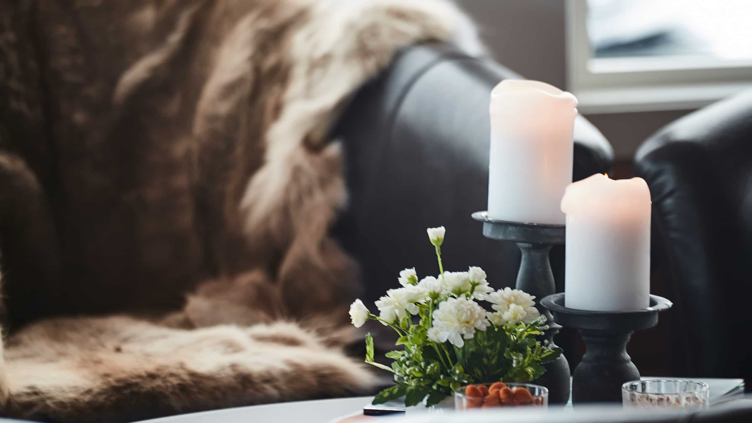 Flower vase and candle on the wooden tray on the coffee table over sofa